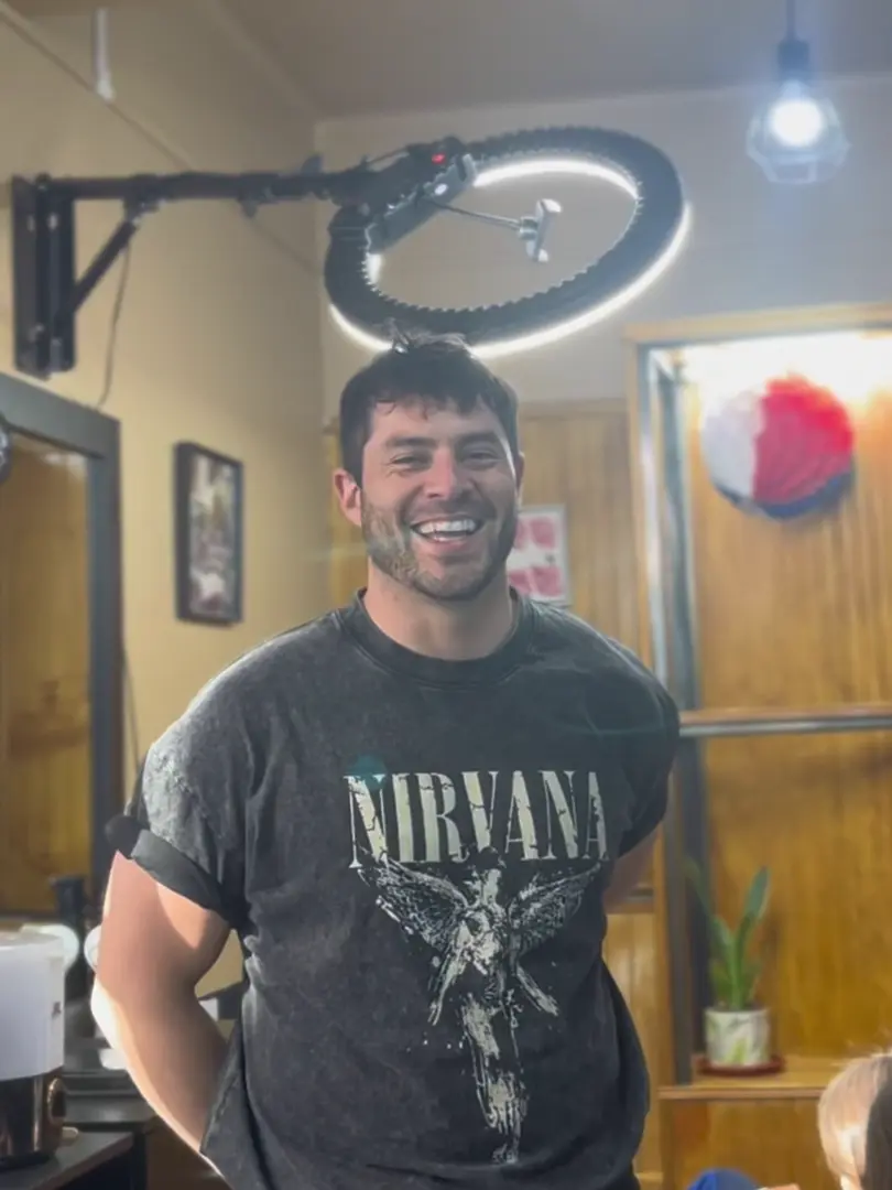 Barbero sonriendo dentro del local, bajo una luz circular