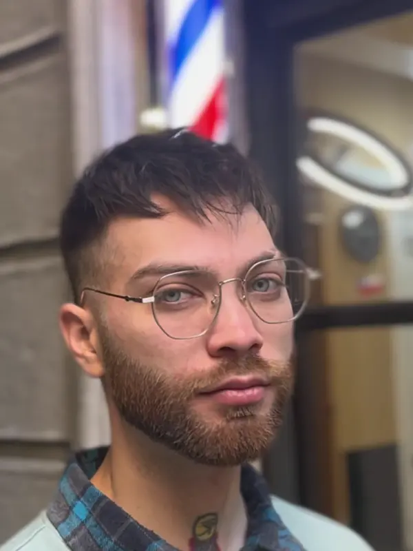 Corte texturizado con barba perfilada, frente al poste de barbero